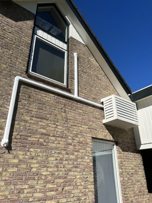 Gevel van huis met airco-unit en pijpen tegen blauwe lucht